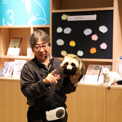 たぬきのぬいるぐみを手にもって説明を行う男性