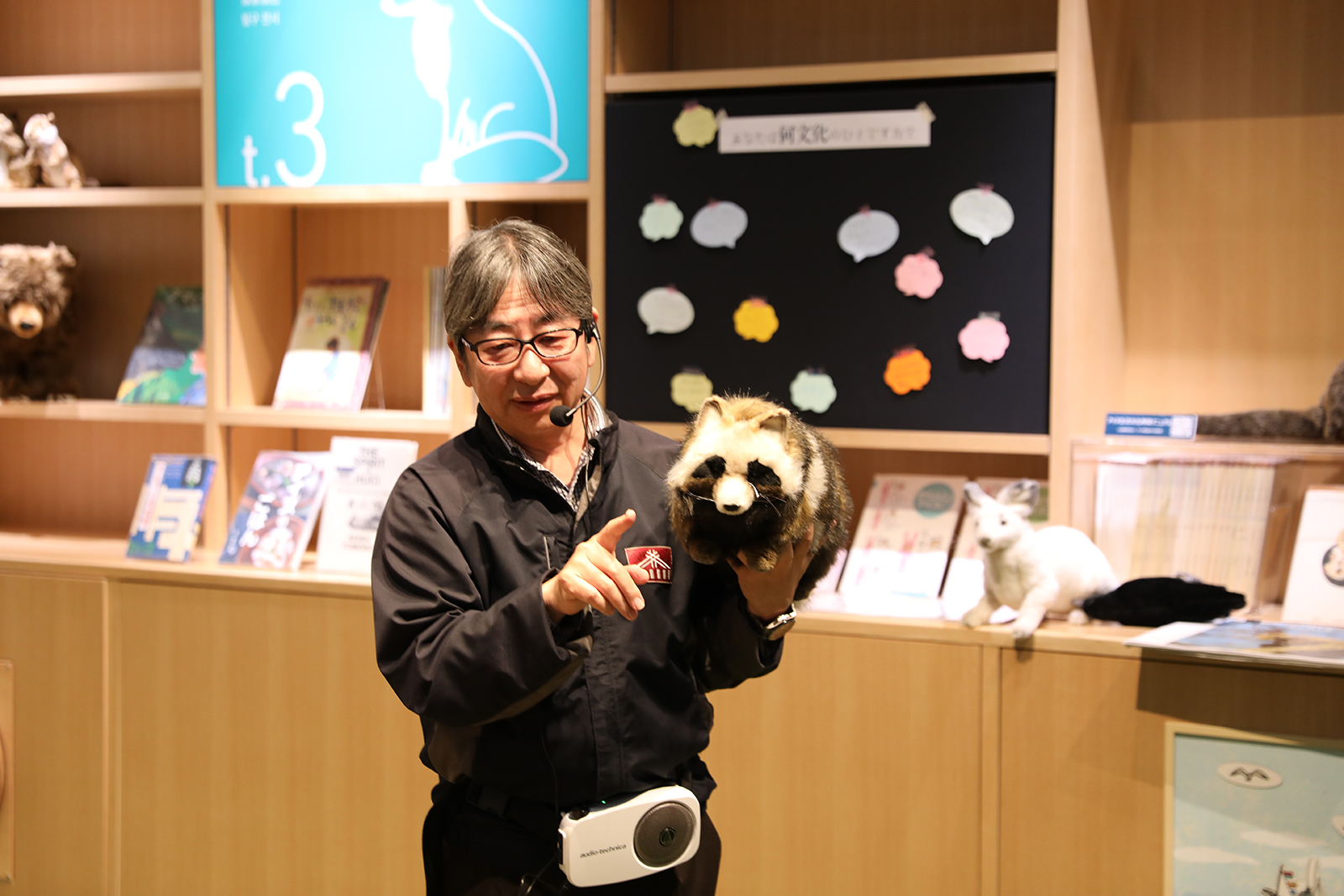 たぬきのぬいるぐみを手にもって説明を行う男性