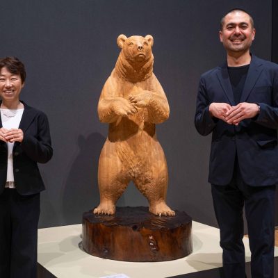 熊の木彫りの横でポーズをとる男性と女性