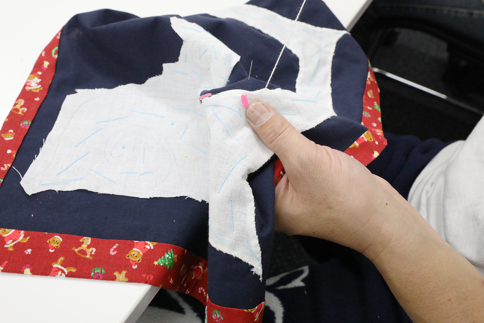 白・紺・赤の布に刺繍を行う手元